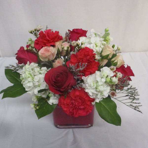 Red and white mixed flower arrangement in a square glass vase