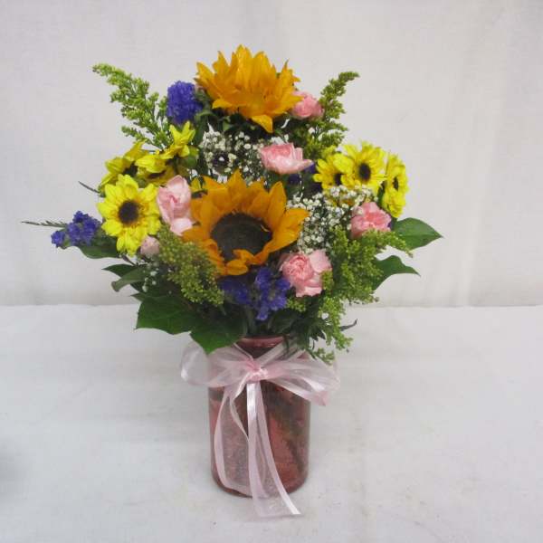 Bouquet of sunflowers, pink roses, and blue flowers in a glass vase