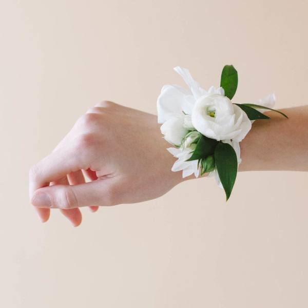 White floral wrist corsage worn on a hand against a soft beige background