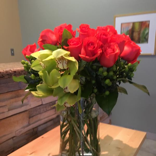 Red roses and green orchids arranged in a clear glass vase