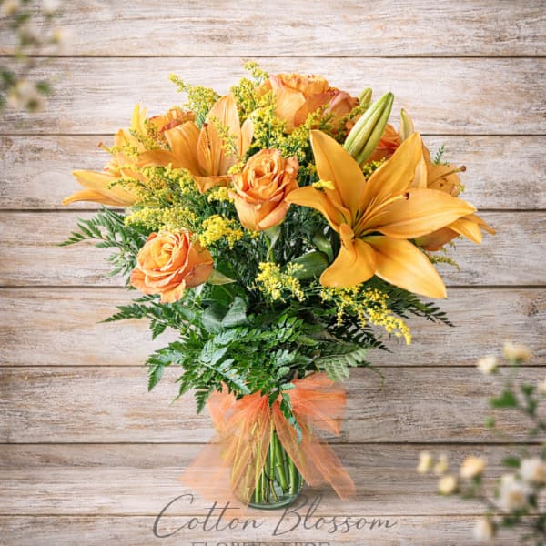 Orange roses and lilies in a glass vase with a sheer ribbon
