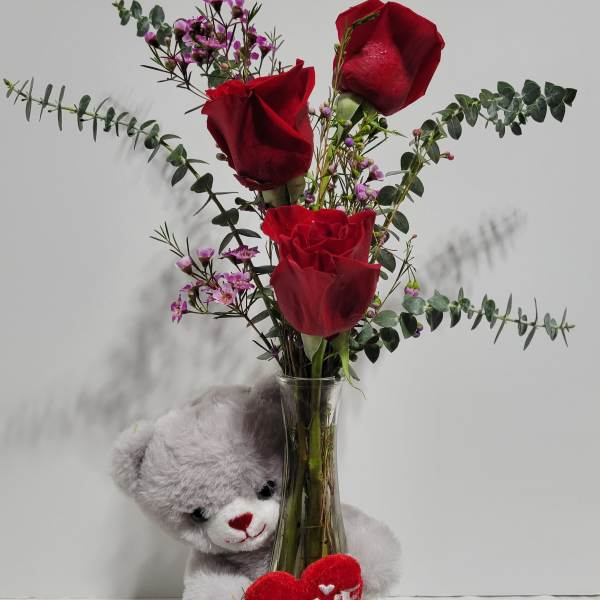 Red roses in a glass vase with a teddy bear and heart decoration