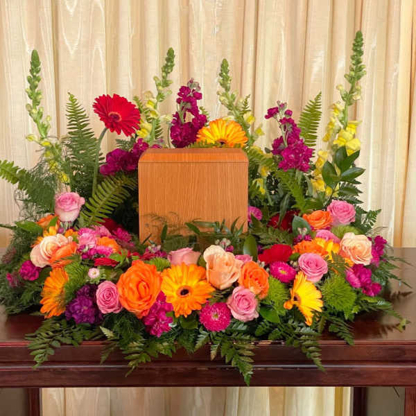 Colorful floral arrangement surrounding a wooden urn on a table