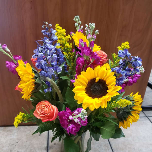 Colorful mixed bouquet with sunflowers, roses, and blue flowers in a glass vase