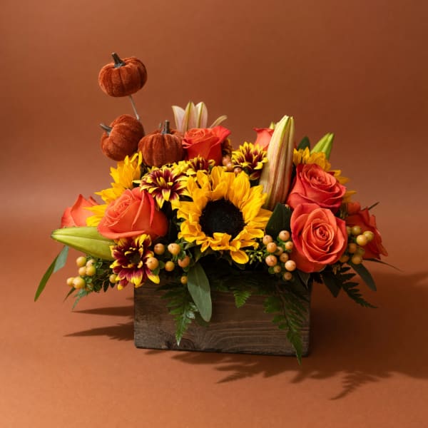 Autumn floral arrangement with sunflowers, roses, and decorative pumpkins in a wooden box