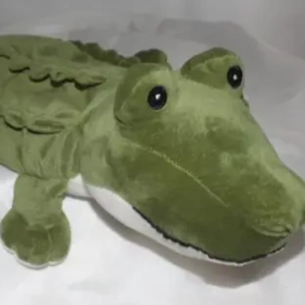 Green plush alligator toy lying on white fabric