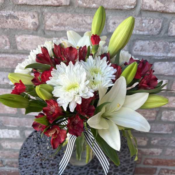 Red and white mixed flower bouquet in a clear glass vase with a striped ribbon bow
