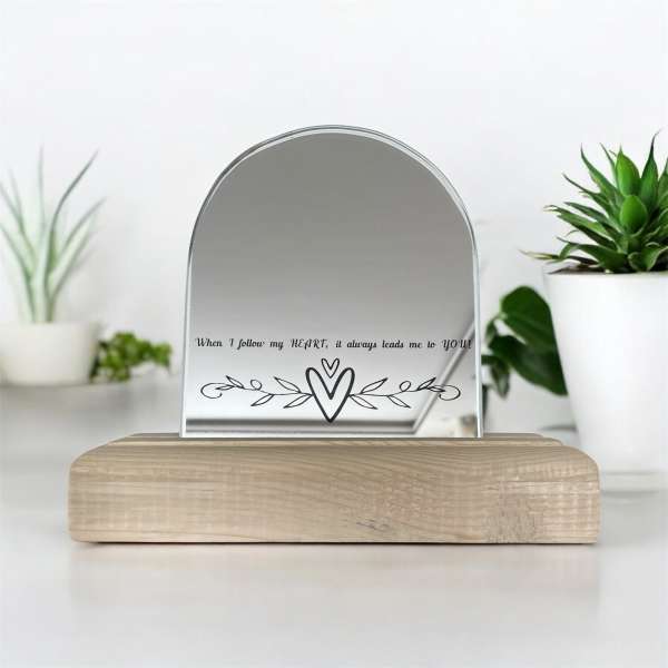 A small arched mirror on a wooden base with a heart design and text.