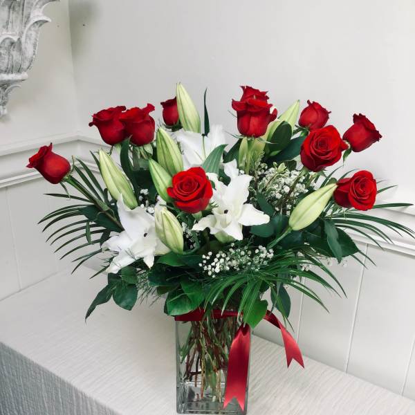 Red roses and white lilies in a clear glass vase with a red ribbon