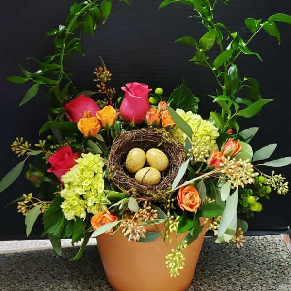 Floral arrangement with roses and hydrangea in a pot, topped with a bird nest and eggs