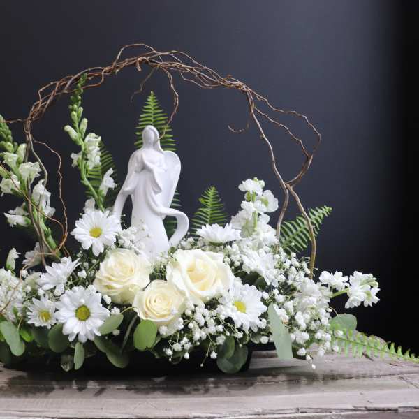 White floral arrangement with roses and daisies around a figurine
