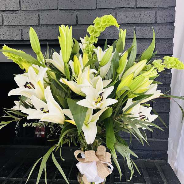 White lilies and green blooms in a glass vase with a burlap bow