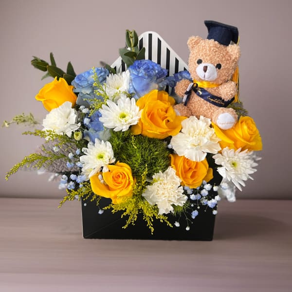 Yellow and blue flower arrangement with a teddy bear in a graduation cap