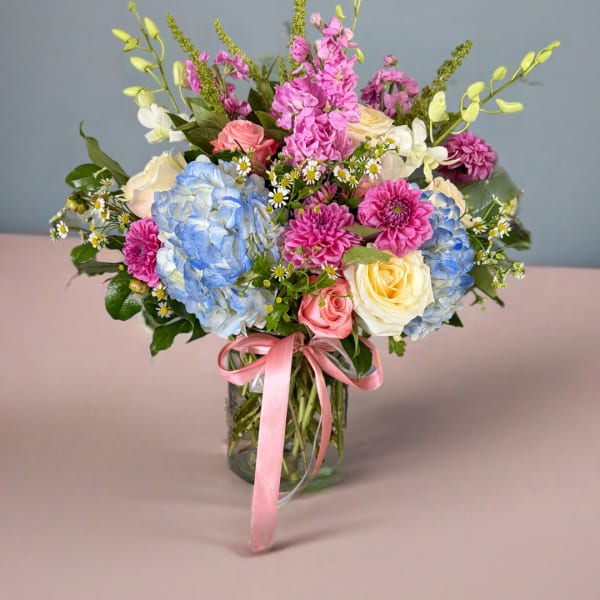 Mixed bouquet of roses, hydrangeas, and pink blooms in a glass vase
