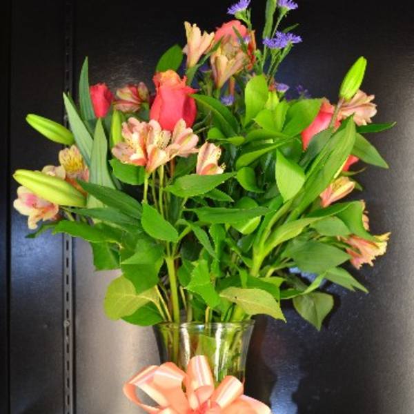 Bouquet of pink lilies and purple filler flowers in a glass vase with a peach ribbon