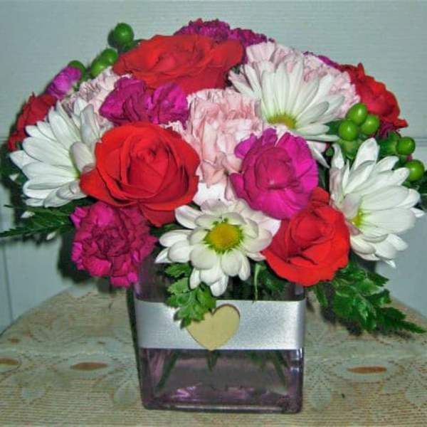 Bouquet of red roses, white daisies, and pink carnations in a square vase