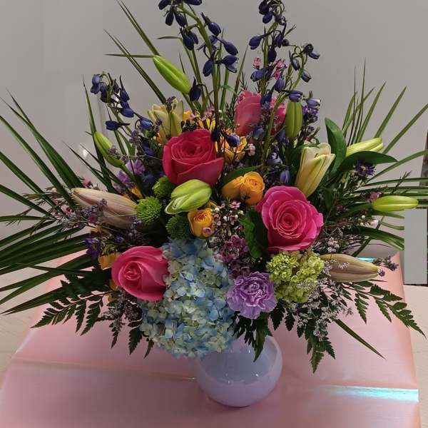 Colorful mixed bouquet in a white vase with roses, lilies, and hydrangea