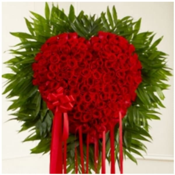 Heart-shaped red rose arrangement with a red ribbon and green foliage