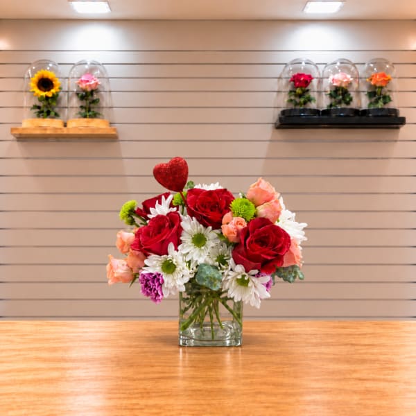 Bouquet of red roses, white daisies, and peach flowers in a glass vase