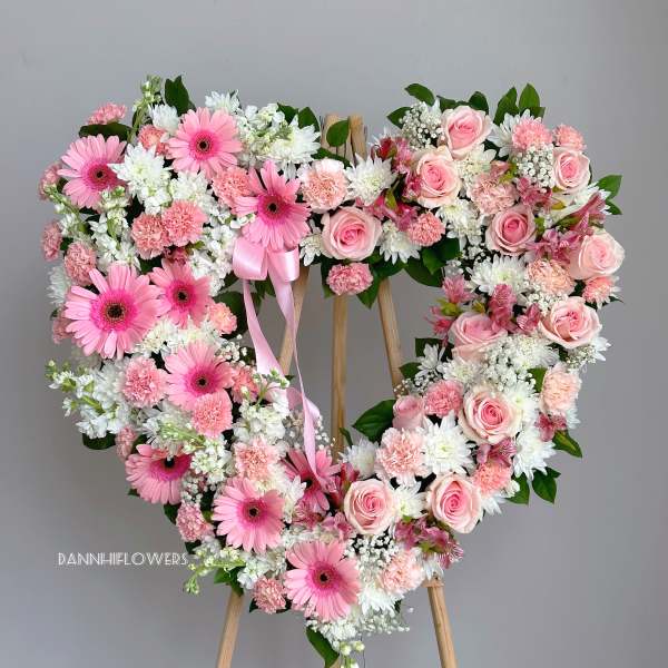 Heart-shaped floral wreath with pink roses and gerbera daisies on an easel