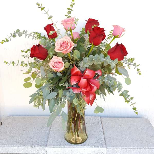 Red and pink roses in a glass vase with a red ribbon