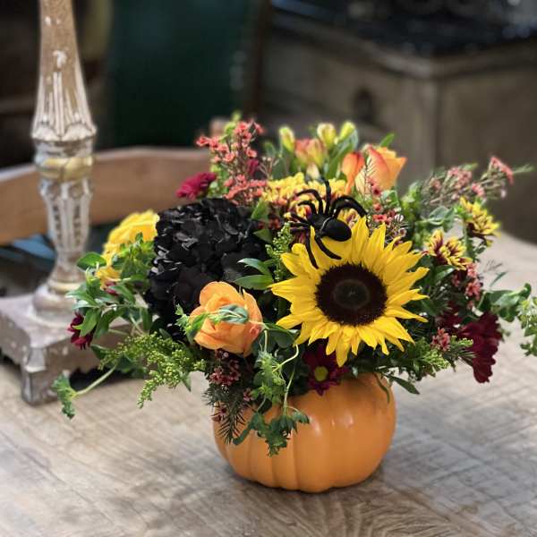 Fall floral arrangement in a pumpkin container with a sunflower and orange roses