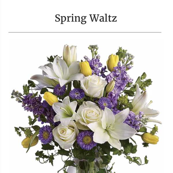 White lilies, roses, and purple flowers in a clear glass vase