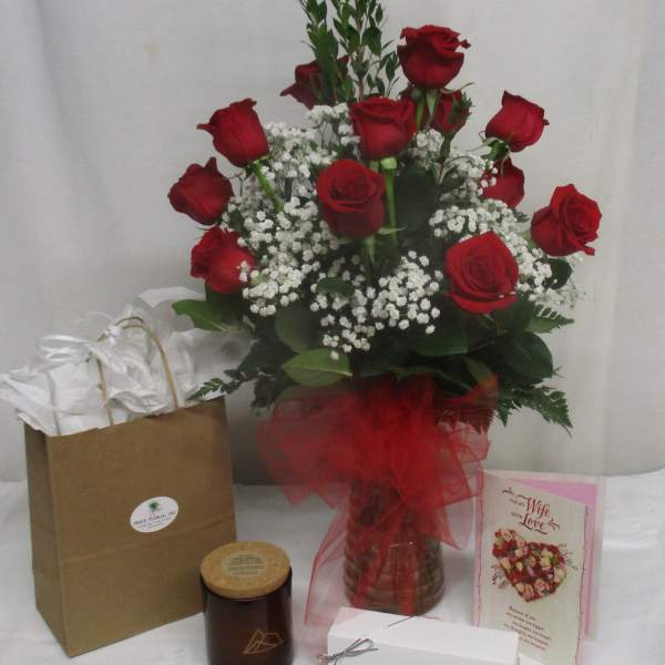 Red roses arranged in a glass vase with baby's breath and gift items nearby