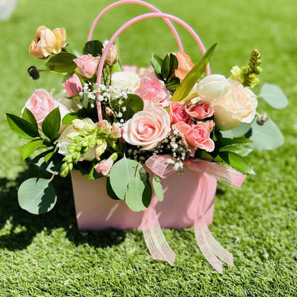 Pink and white roses in a pink handled gift box on grass