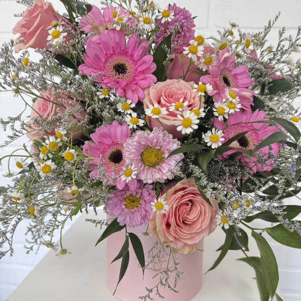 Pink roses and gerbera daisies in a pink hatbox with small white daisies