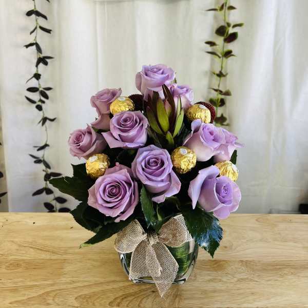 Lavender rose arrangement in a glass vase with gold-wrapped chocolates