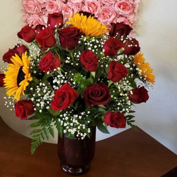 Bouquet of red roses and yellow sunflowers in a dark glass vase