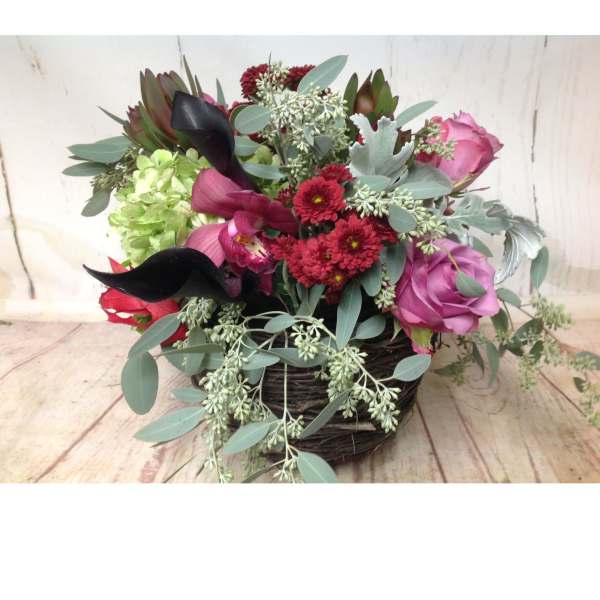 Low basket arrangement with pink roses, red mums, dark calla lilies, green hydrangea, and cascading eucalyptus.