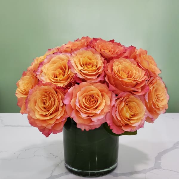 Orange and pink roses arranged in a dark glass vase