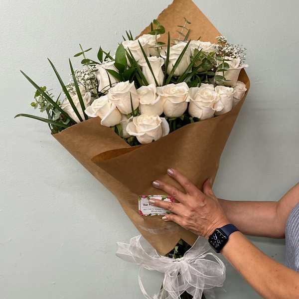 Bouquet of white roses wrapped in brown paper with a white ribbon