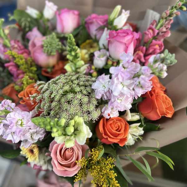 Mixed bouquet of pink, orange, and lavender flowers wrapped in brown paper