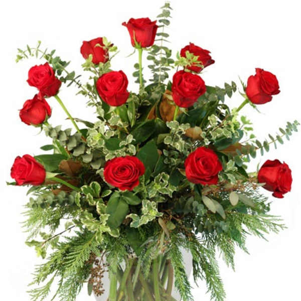 Tall arrangement of long-stem red roses with assorted foliage in a clear glass vase.