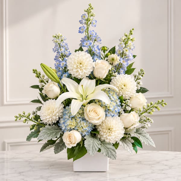 White lilies, roses, and blue flowers arranged in a white vase