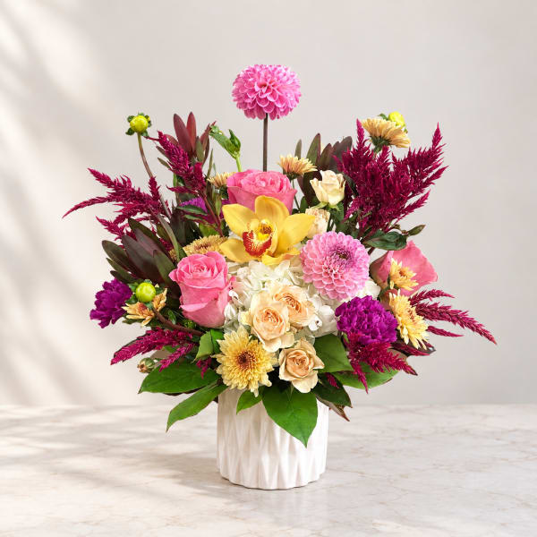 Colorful flower arrangement in a white vase with pink, yellow, and cream blooms