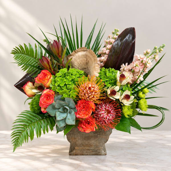 Tropical floral arrangement in a rustic vase with roses and protea