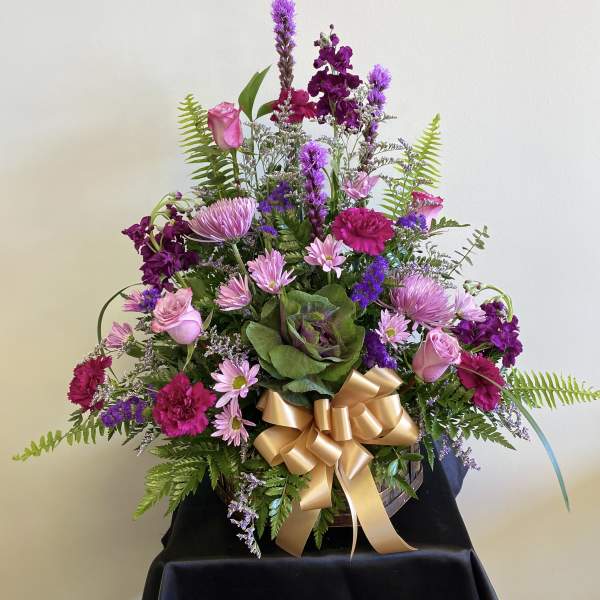 Pink and purple mixed flower arrangement with a gold ribbon in a basket