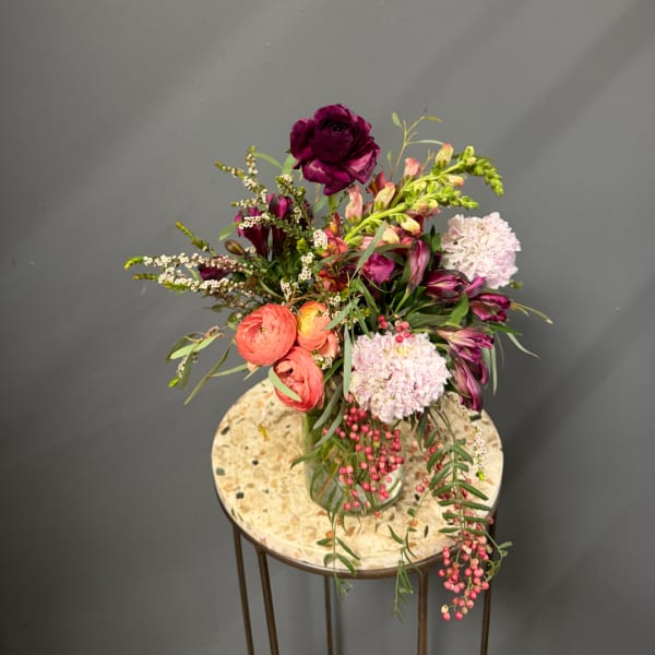 Mixed bouquet in a glass vase with deep purple, coral, and pale pink flowers
