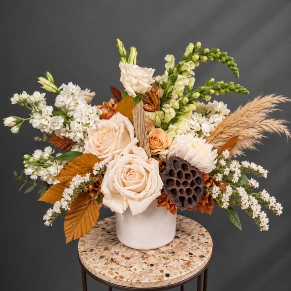 Cream rose arrangement in a white vase with white blooms and dried grasses