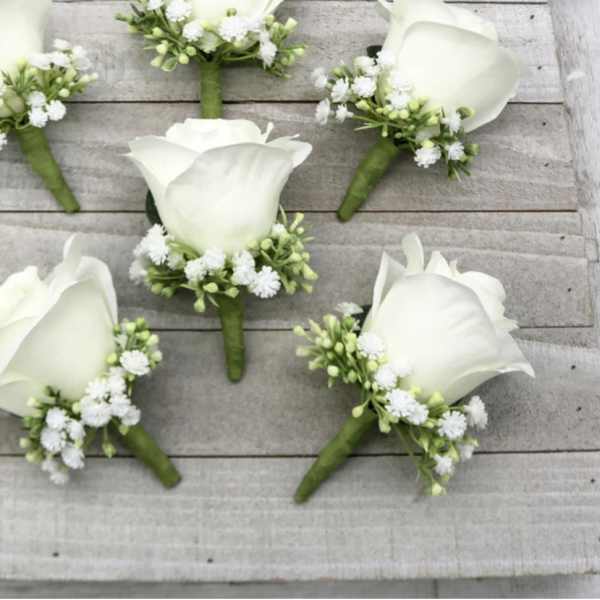 Set of white rose boutonnieres with small white filler flowers on rustic wood boards