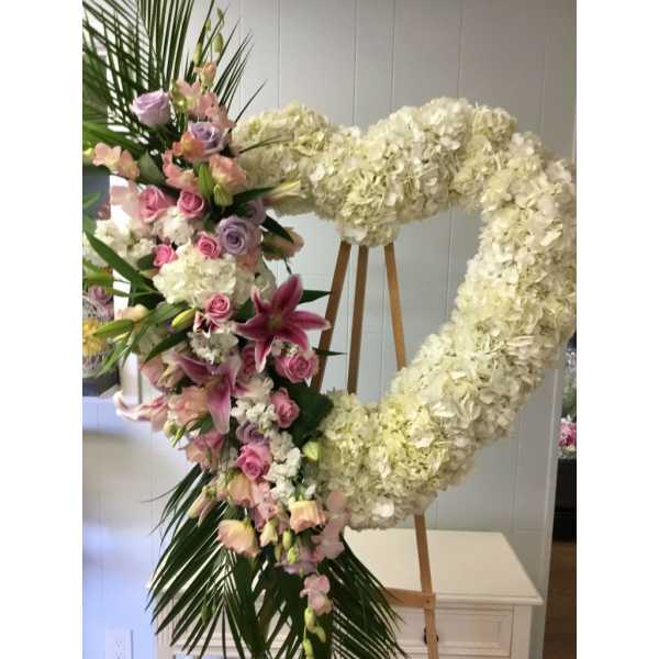 Heart-shaped floral wreath with white hydrangeas, pink roses, and lilies on an easel