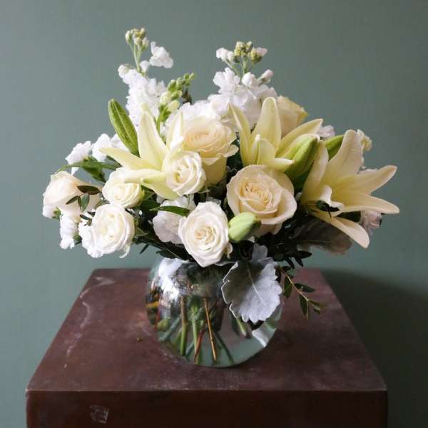 White lilies and roses arranged in a round glass vase