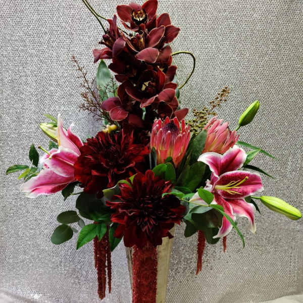 Tall floral arrangement with burgundy orchids and pink lilies in a gold vase