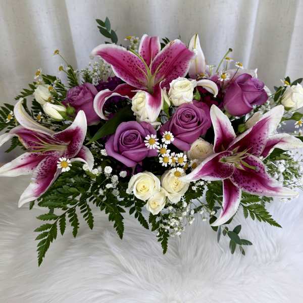 Pink lilies and purple roses arranged with small white flowers.