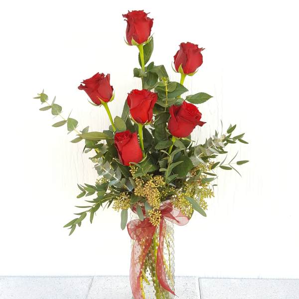 Tall bouquet of red roses in a clear glass vase with ribbon