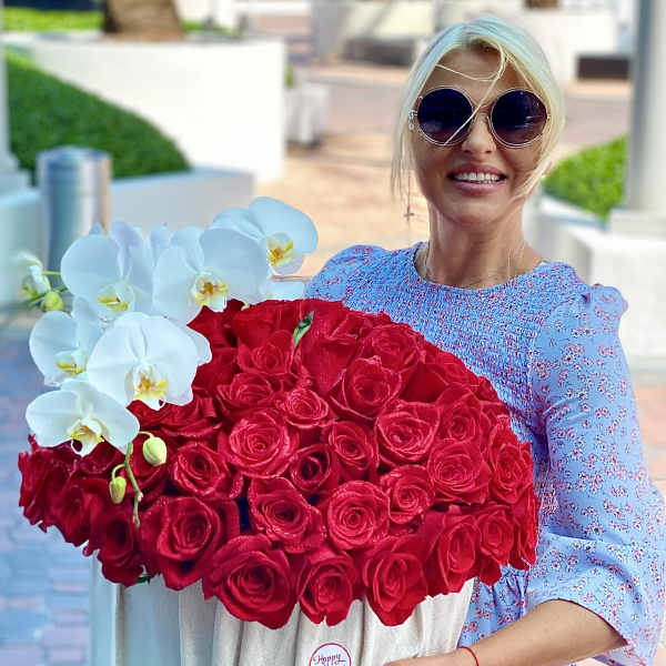 Woman holding a large box of red roses with white orchids